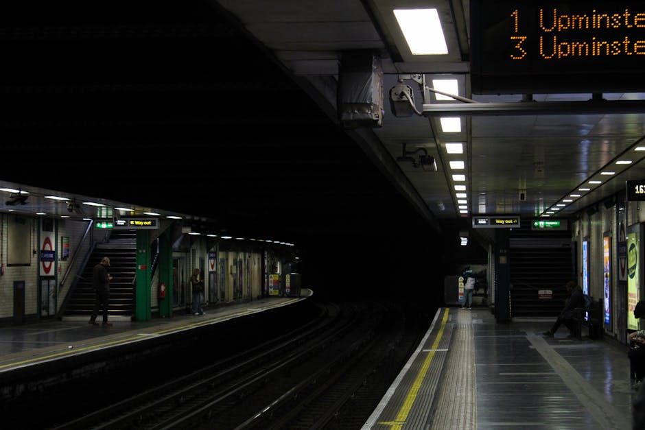 Photograph of a London Underground station platform during sunset, with train tracks curving towards the tunnel illuminated by warm sunlight. The platform has tactile paving with yellow safety lines a